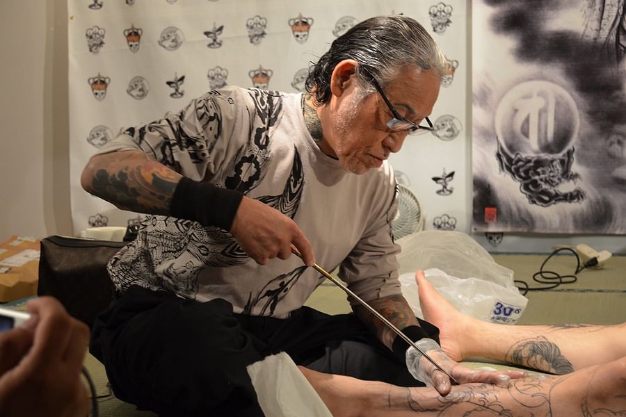 Hand-poking tattoo artist at work, using a needle attached to a rod or handle
